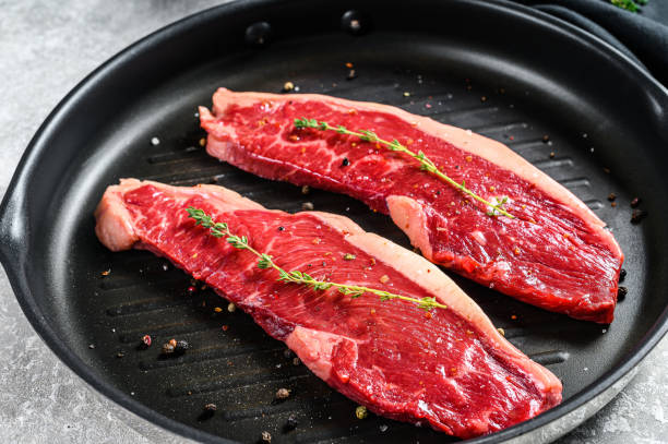istock Raw marbled beef steak on a grill pan, ingredients for cooking. Gray background. Top view 1291718005