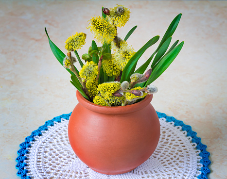 The ceramic vase with branches of a blossoming willow is located on a table on a lacy napkin.