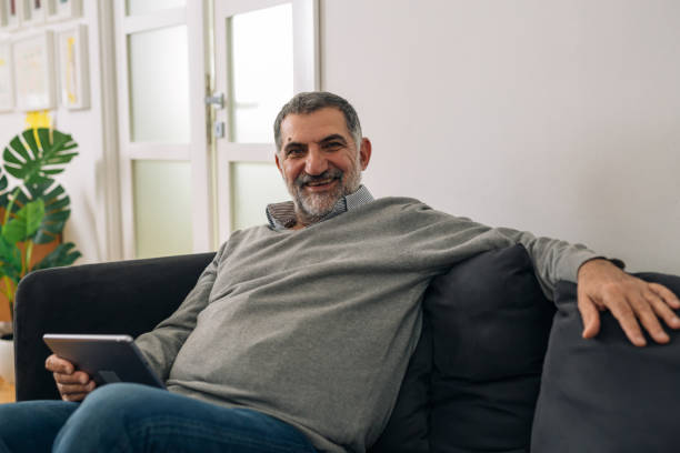 istock middle aged man sitting on sofa and using tablet at home 1291721582