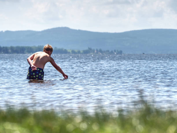 istock Boy Stay In Cold Lake With Water Under Knee And Test Temperature. Cold Spring Day For Swim. 1291724053