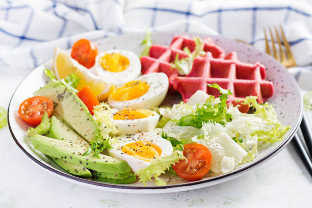 istock Breakfast with beetroot waffles, boiled egg, tomato and slice avocado on white background. Appetizers, snack, brunch. Healthy food. 1291724455