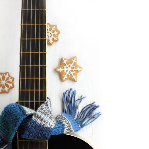 knitted blue scarf tied on the neck of an acoustic guitar on a light background with blurred silhouettes of gingerbread cookies