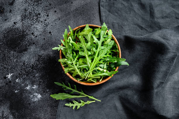 istock Fresh arugula in a wooden bowl. Black background. Top view 1291730093