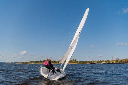 A young sailing instructor conducts a class with two female novices on a river with a beautiful landscape