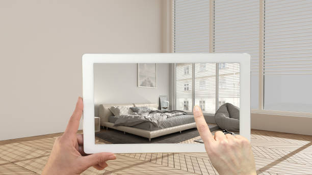 istock Augmented reality concept. Hand holding tablet with AR application used to simulate furniture and design products in empty interior with parquet floor, modern bedroom with decors 1291731763