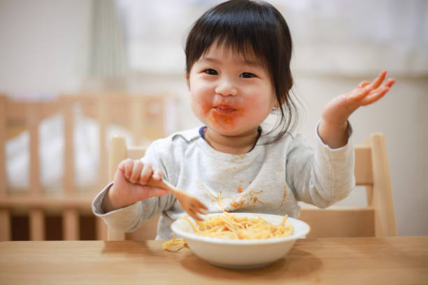 une fille qui se salit les vêtements avec de la nourriture - child eating pasta spaghetti photos et images de collection