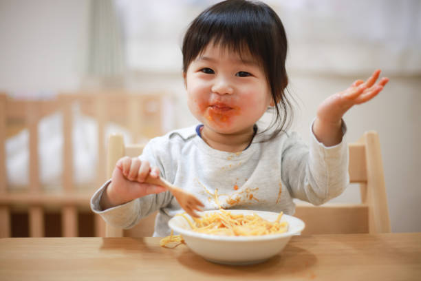 食べ物で服を汚す女の子 - child eating pasta spaghetti ストックフォトと画像