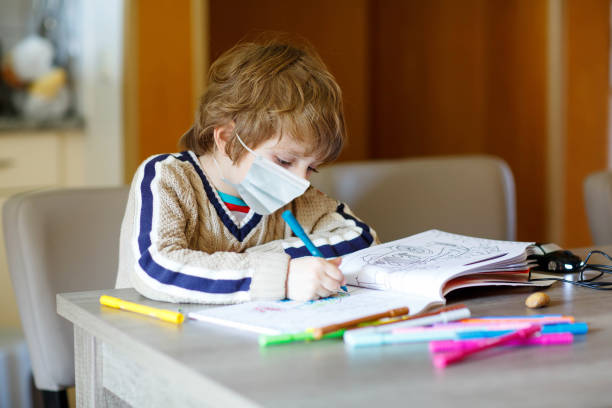 istock Hard-working school kid boy with medical mask learning during quarantine time from corona pandemic disease. Child on home schooling in coronavirus covid time, schools closed. Homeschooling concept 1291737377
