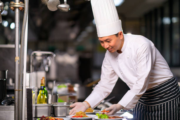เชฟชายชาวเอเชียนําเสนอจานในห้องครัว โฟกัสที่เลือก ภาพสต็อก