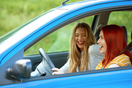 Blond laughing with her redhead best friend driving blue car in nature