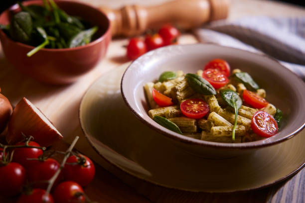 Pesto penne pasta with cherry tomatoes and basil in a bowl on a rustic table