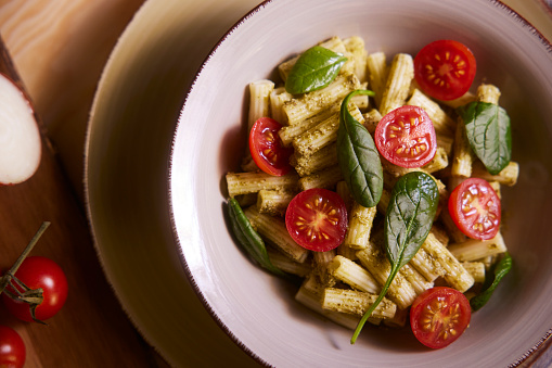 Top-view of bowl of penne pasta with pesto cherry tomatoes and basil