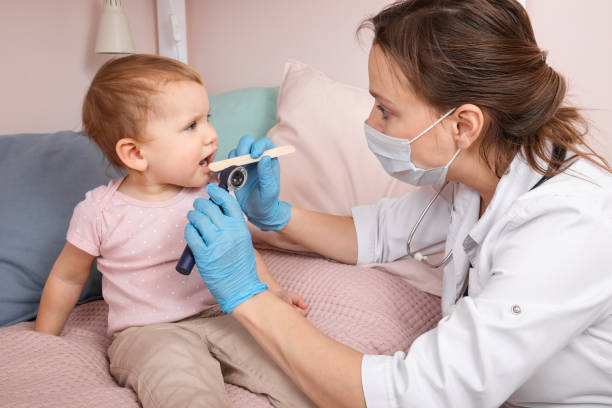 Pediatrician checking sore throat of baby girl at home during coronavirus lockdown stock photo