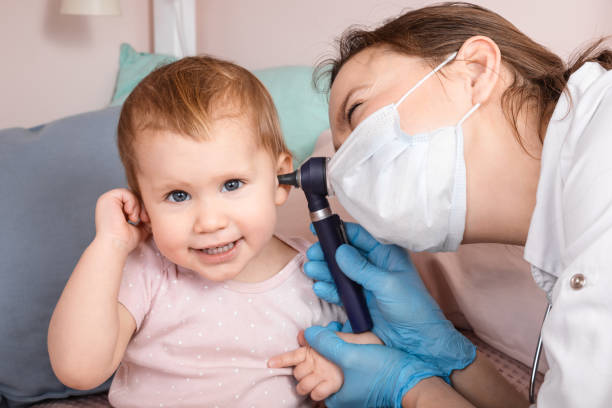 pediatrician checking ear of baby girl with otoscope performing ent exam at home during lockdown - young ears imagens e fotografias de stock