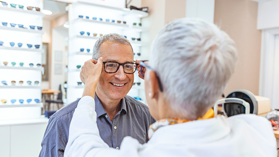 Happy Mature man trying on glasses in optometrists shop.
