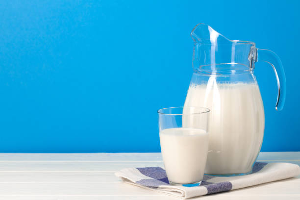 istock Glass and pitcher of milk against blue background 1291744934