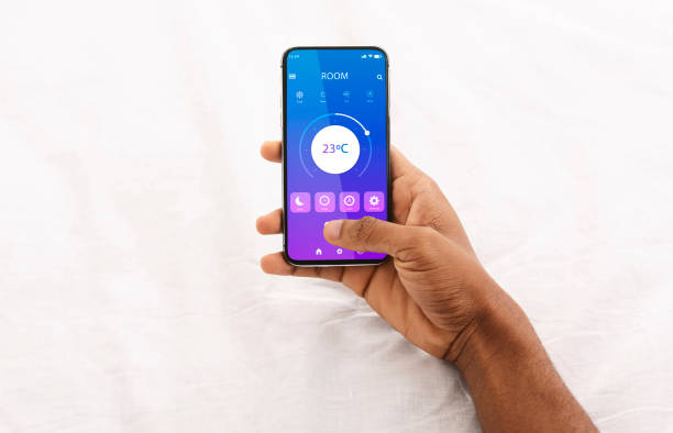 istock Black man holding cellphone with smart home application in bed, regulating temperature, creating cozy environment 1291747890