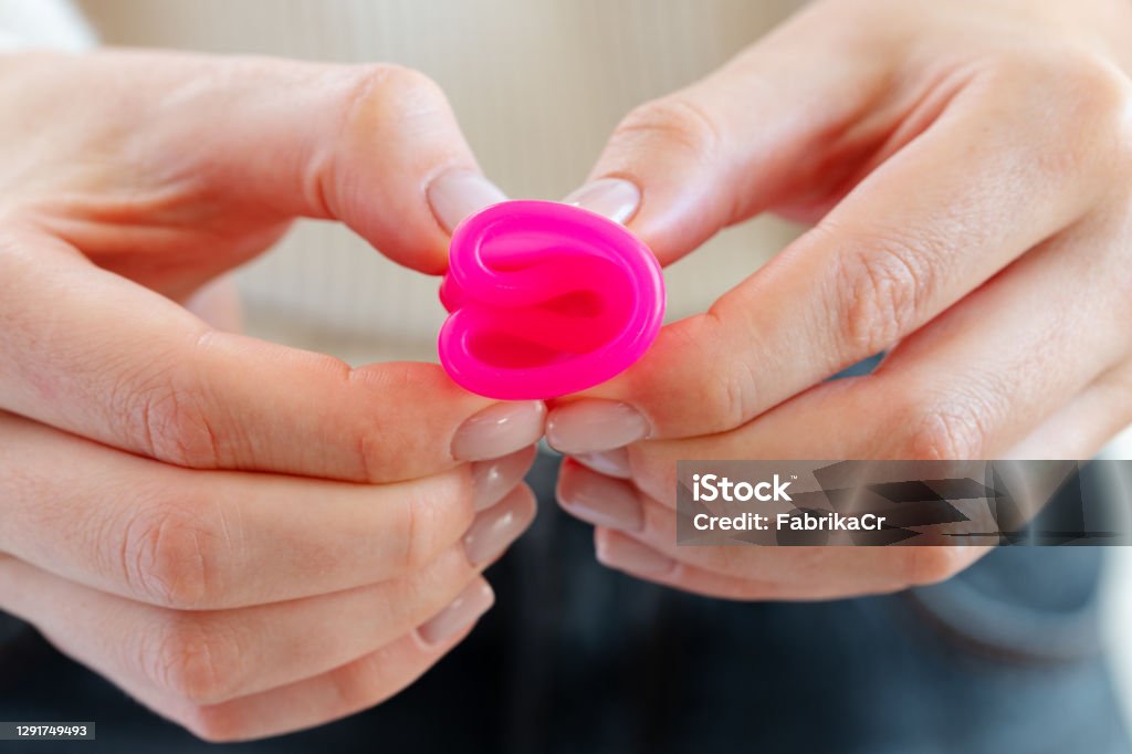 Woman in white sweater holding pink menstrual cup in hands close up Woman in white sweater holding pink menstrual cup in hands close up photo Cup Stock Photo