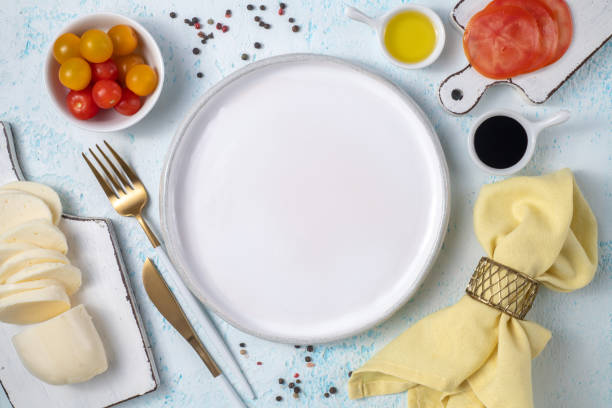 istock Empty white plate surrounded by cutlery and fresh vegetables top view on blue background 1291751082