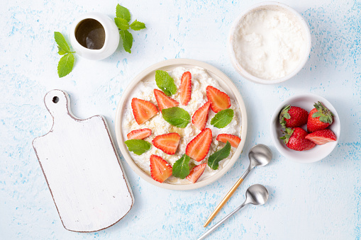 Soft cream cheese or organic curd with fresh strawberries and mint leaves top view on light blue background