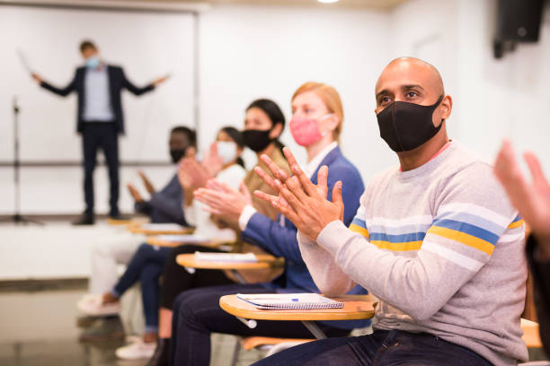 istock Hispanic man in protective mask applauding during business seminar 1291753435
