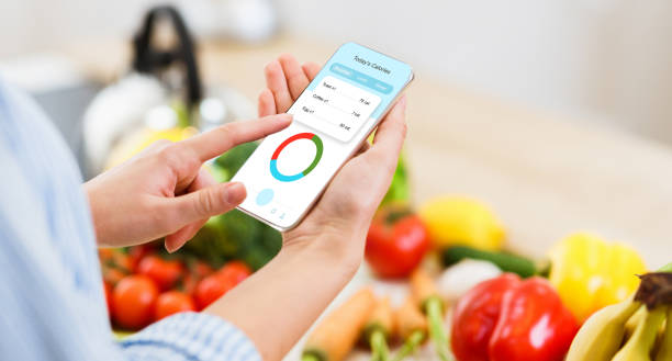 mulher usando aplicativo de contador de calorias em seu smartphone enquanto cozinha almoço saudável - fat cell - fotografias e filmes do acervo