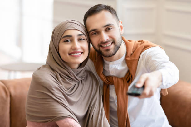 istock Young Muslim Spouses Watching Television Sitting On Couch At Home 1291754791