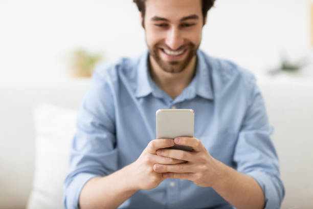istock Happy Guy Using Smartphone Texting Sitting On Couch At Home 1291754878
