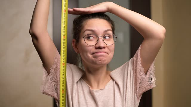A young woman shows joy at her growth by holding a measuring tape next to her