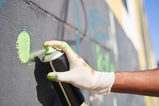 Close up of the hand of multiracial man wearing dirty disposable gloves holding spray paint can while drawing live murales. Urban lifestyle and artist concept