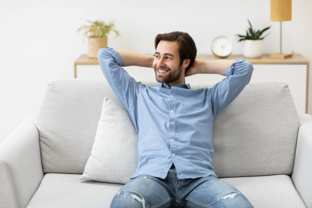 istock Relaxed Guy Sitting Holding Hands Behind Head On Sofa Indoor 1291760089