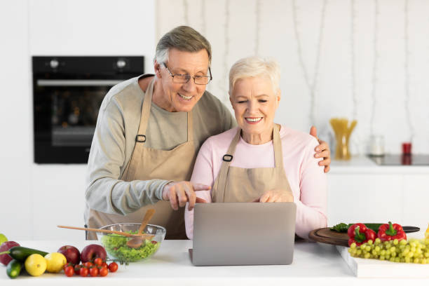 istock Senior Couple Cooking And Using Laptop Preparing Dinner In Kitchen 1291760763