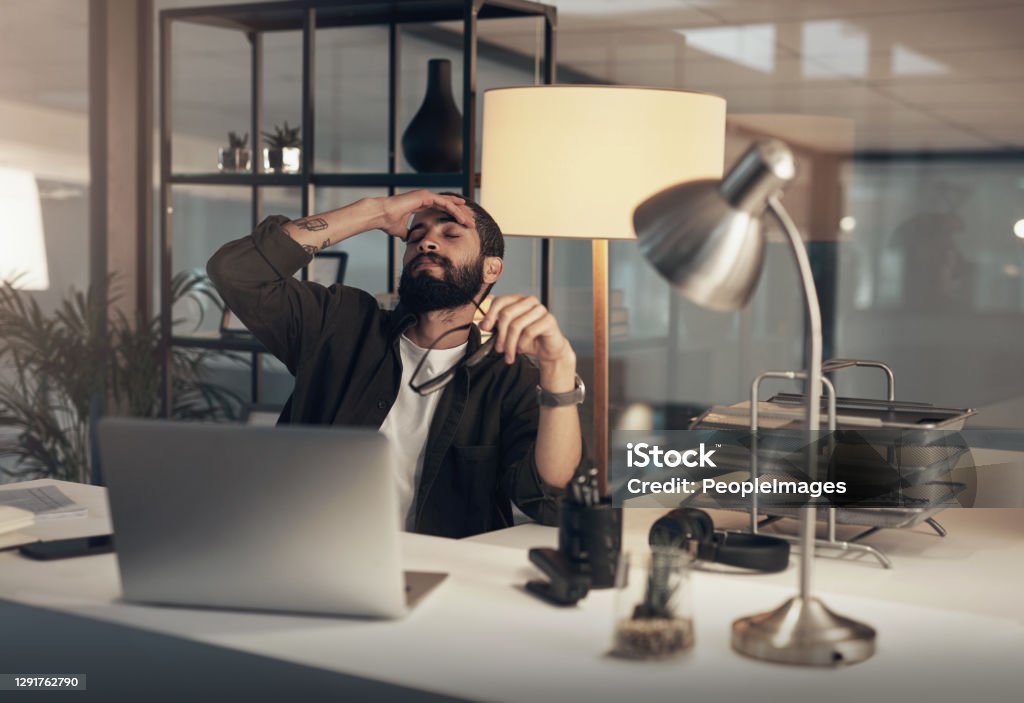 The night just got a lot longer Shot of a young businessman feeling stressed while working late at night in a modern office Mental Health Stock Photo