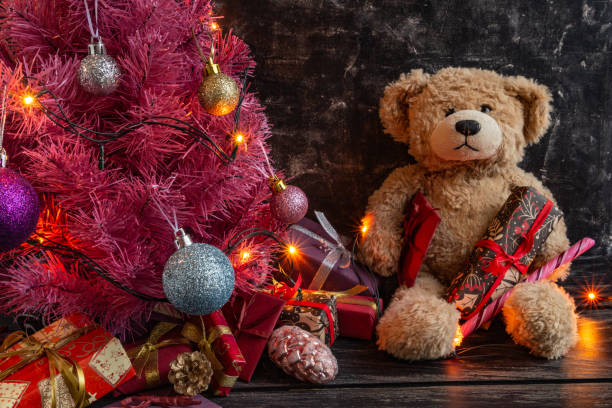 istock Atmospheric Christmas or New Year composition, pink christmas tree on black background, teddy bear, gifts. Copy space 1291762998