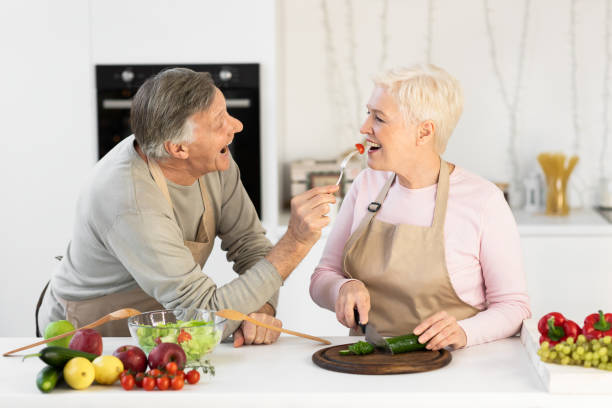 istock Cheerful Elderly Husband Feeding Wife Tasting Dinner Cooking In Kitchen 1291764197