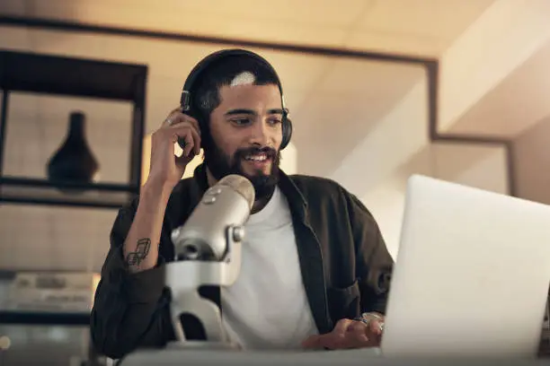 Shot of a young man using a headset, microphone and laptop during a late night at work