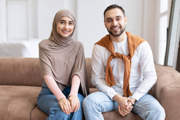 istock Muslim Couple Sitting On Sofa Smiling To Camera At Home 1291765241