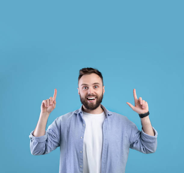 istock Excited bearded guy pointing up at blank space over blue studio background 1291765378