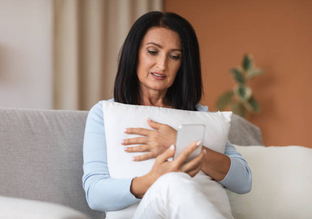 istock Mature woman using mobile phone, holding pillow 1291766565