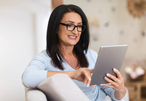 istock Mature woman sitting on couch and using tablet 1291766624