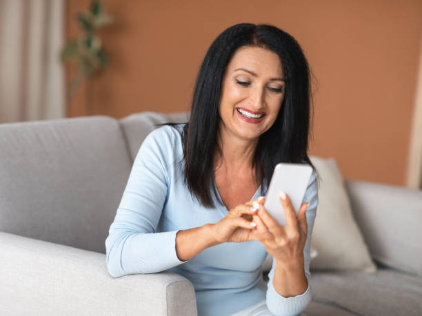 istock Happy mature woman using smartphone sitting on couch 1291766672
