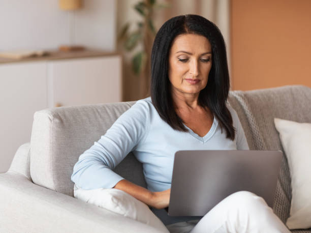 istock Mature woman sitting on couch and working on computer 1291766679