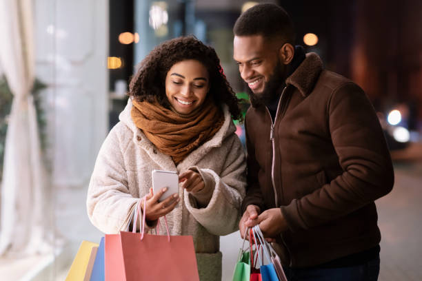 istock Happy afro couple using smartphone with many shopping bags 1291766926