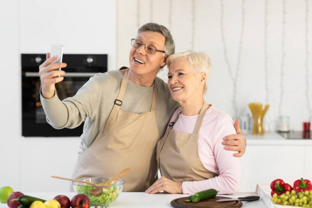 istock Cheerful Senior Couple Making Selfie On Cellphone Cooking In Kitchen 1291767571