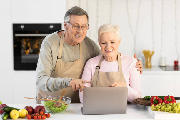 istock Older Couple Cooking Using Laptop In Modern Kitchen At Home 1291767804