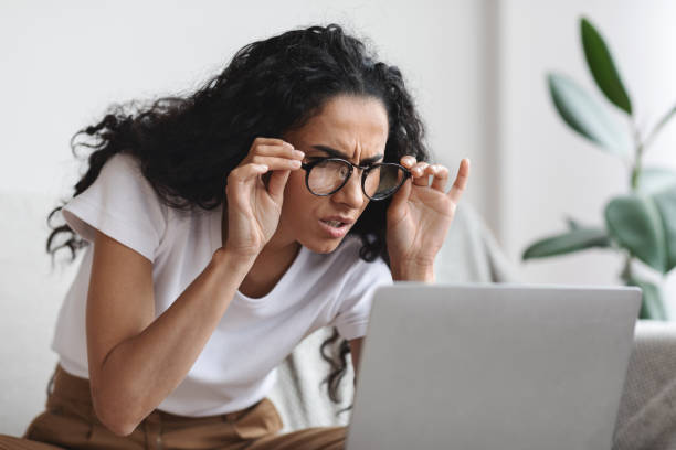 Young woman with bad eyesight using laptop, wearing glasses Young woman freelancer with bad eyesight using laptop, using glasses, home interior, copy space. Curly lady holding her glasses and squinting, looking at laptop screen, having vision troubles squint eyes stock pictures, royalty-free photos & images