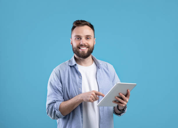 istock Modern technologies and communication. Portrait of happy bearded man using tablet computer over blue background 1291768278