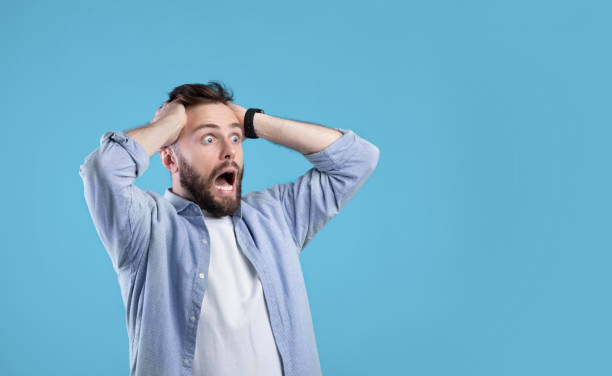 istock Shocked millennial guy shouting and holding his head in disbelief, looking at empty space on blue studio background 1291768469