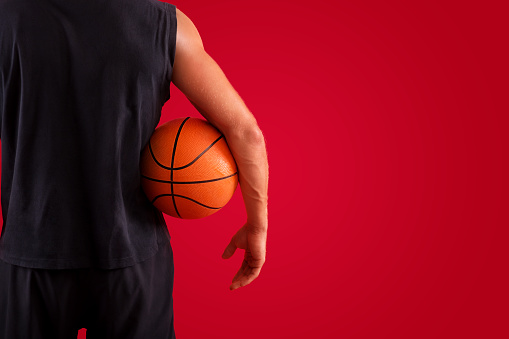Closeup of millennial basketball player holding ball over red studio background, space for text. Back view of young sportsman ready to play streetball match, participate in championship