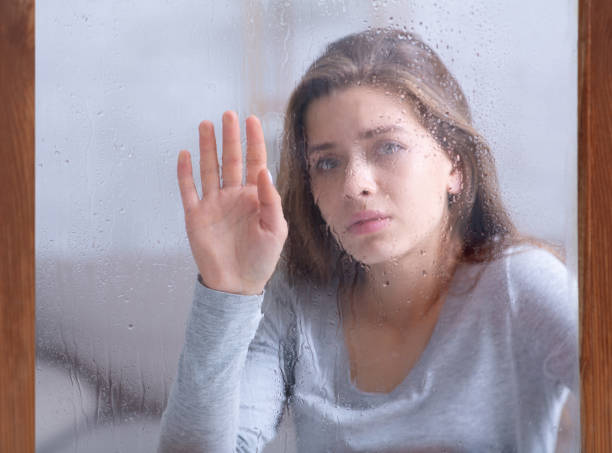 istock Depressed young lady touching window glass with rain drops, feeling unhappy or melancholic 1291771279